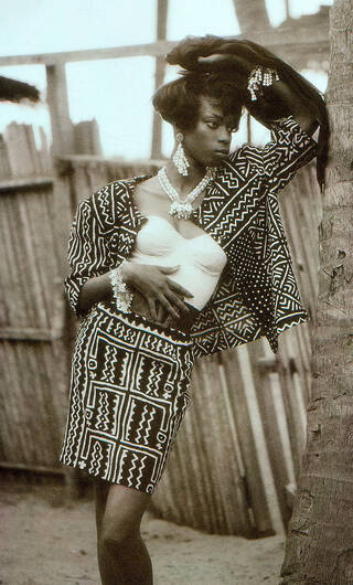 Model posing with arm against a tree. Wearing black skirt and short sleeved jacket with white patterned detailing