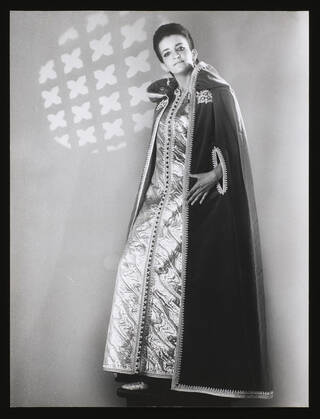 Black and white image of a woman in a long dress and long cape with hood