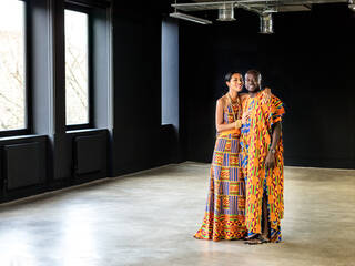Image of man and woman in bright orange outfits ina. black and white studio