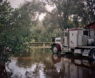 Boy stood in flooded scene next to large lorry